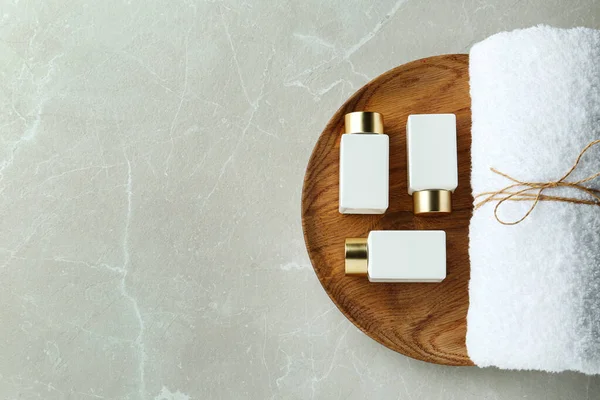 Vue du dessus du plateau en bois avec bouteilles cosmétiques et serviette sur table en marbre gris clair, espace pour le texte. Traitement spa — Photo