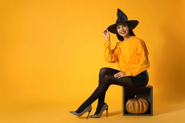 Schöne Frau im Hexenkostüm zur Halloween-Party mit Kürbis vor gelbem Hintergrund, Platz für Text — Stockfoto
