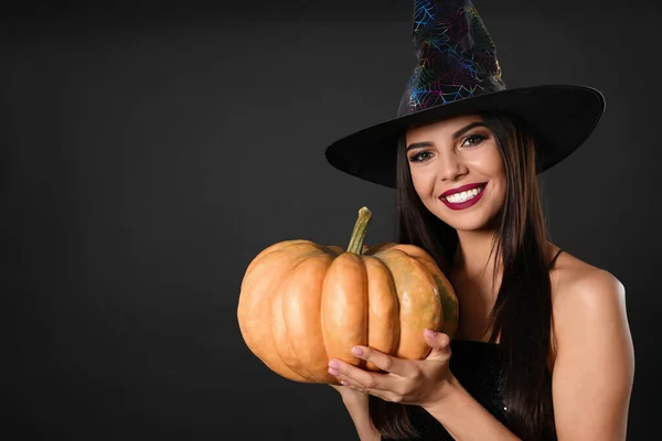 Beautiful woman wearing witch costume with pumpkin for Halloween party on black background, space for text — ストック写真