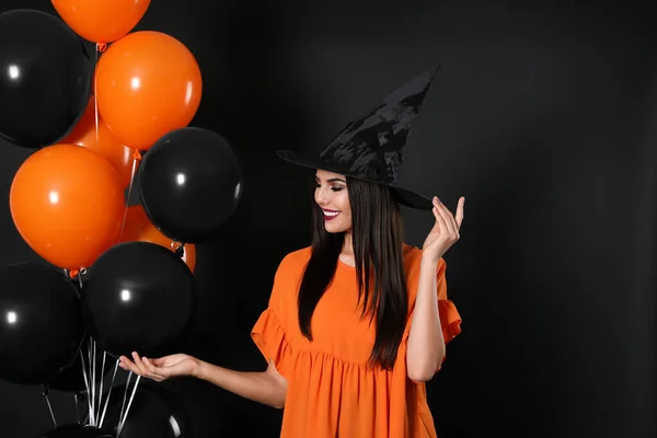 Hermosa mujer con traje de bruja con globos para la fiesta de Halloween sobre fondo negro —  Fotos de Stock