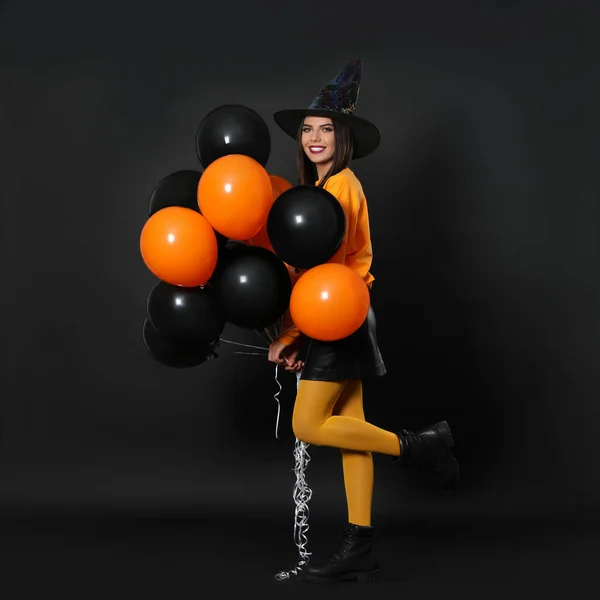 Hermosa mujer con traje de bruja con globos para la fiesta de Halloween sobre fondo negro, espacio para el texto —  Fotos de Stock