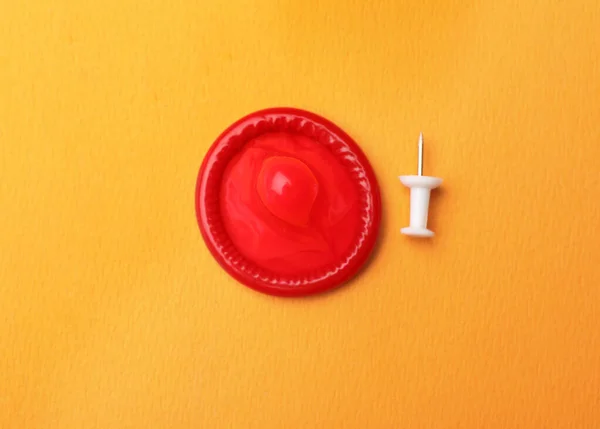Czerwony prezerwatywa i pin na pomarańczowym tle, płaski leżak — Zdjęcie stockowe