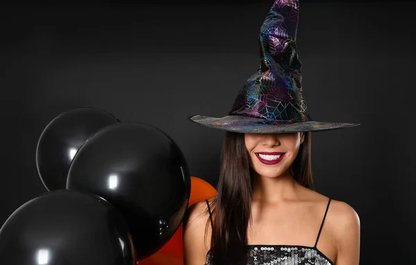 Belle femme portant costume de sorcière avec des ballons pour la fête d'Halloween sur fond noir — Photo