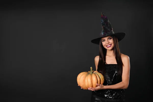 Mulher bonita vestindo traje de bruxa com abóbora para festa de Halloween em fundo preto, espaço para texto — Fotografia de Stock