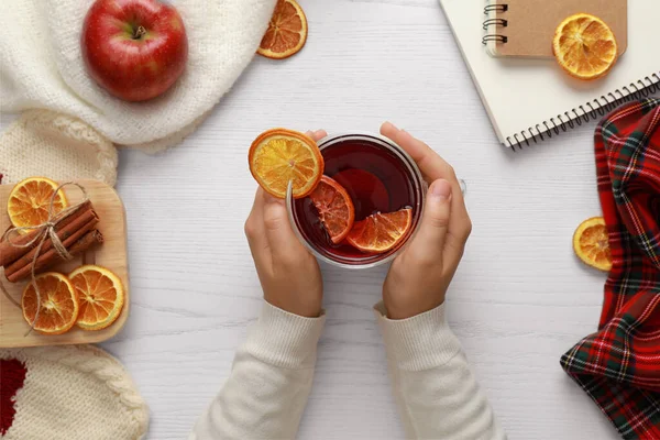 Mujer sosteniendo taza de té caliente en la mesa de madera blanca, vista superior. Acogedor invierno — Foto de Stock