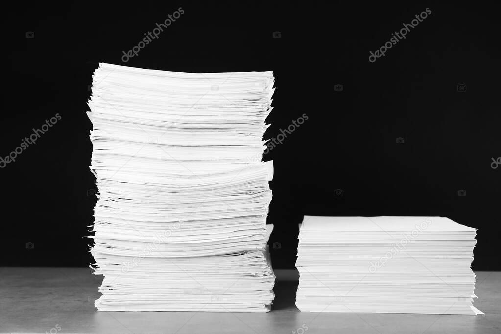 Stacks of blank paper on grey stone table against black background