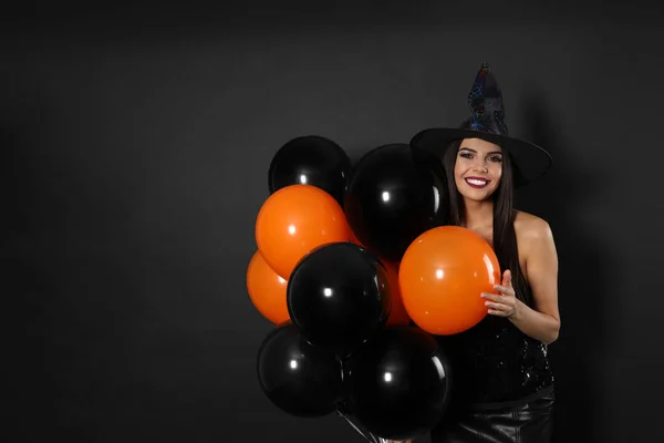 Hermosa mujer con traje de bruja con globos para la fiesta de Halloween sobre fondo negro, espacio para el texto —  Fotos de Stock