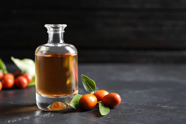 Glass bottle with jojoba oil and seeds on grey stone table against dark background. Space for text