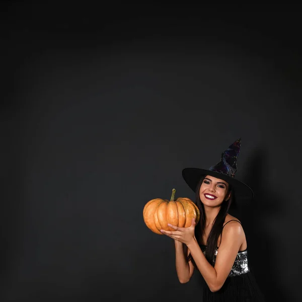 Hermosa mujer con traje de bruja con calabaza para la fiesta de Halloween sobre fondo negro, espacio para el texto —  Fotos de Stock