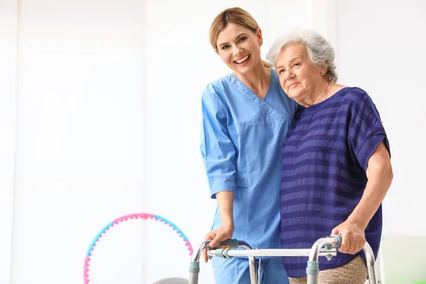 Cuidador ayudando a anciana con marco para caminar en interiores —  Fotos de Stock