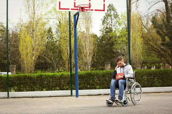 Homem perturbado em cadeira de rodas com bola no chão de esportes — Fotografia de Stock