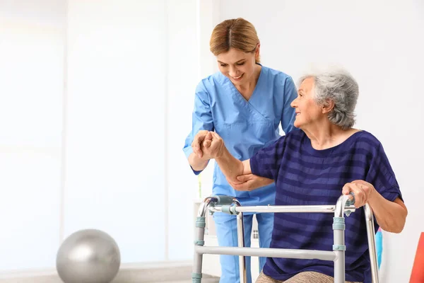 Caretaker helpen oudere vrouw met Walking frame binnenshuis — Stockfoto