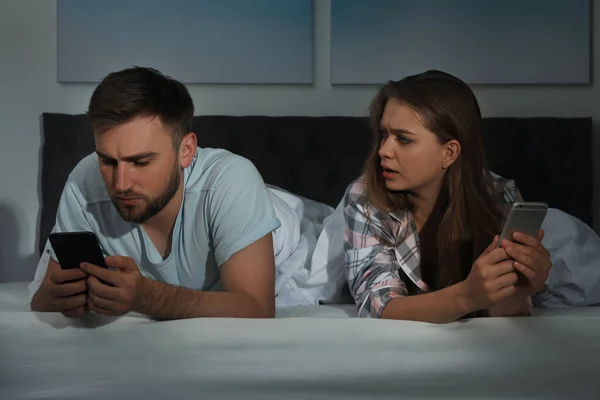 Upset young couple with smartphones in bed at nighttime — 图库照片