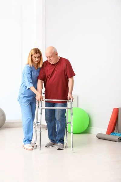 Cuidador ayudando a anciano con marco de caminar en interiores —  Fotos de Stock
