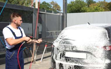 Araba yıkamada yüksek basınçlı su jeti ile otomobili temizleyen genç işçi.