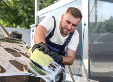 Araba yıkamada süngerle otomobili temizleyen genç işçi.