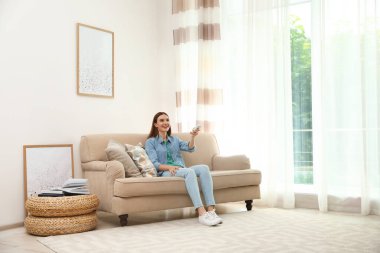 Evdeki klimayı uzaktan kumandayla açan mutlu genç kadın.