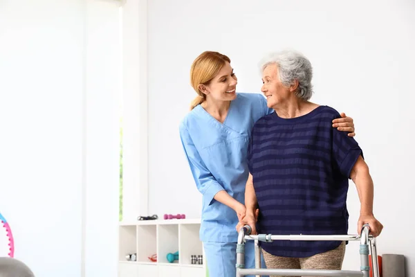 Caretaker helpen oudere vrouw met Walking frame binnenshuis — Stockfoto