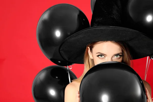 Mulher bonita vestindo traje de bruxa com balões para festa de Halloween no fundo vermelho — Fotografia de Stock