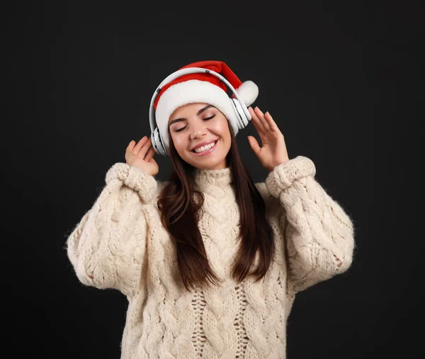 Jeune femme en chapeau Santa écouter de la musique de Noël sur fond noir — Photo