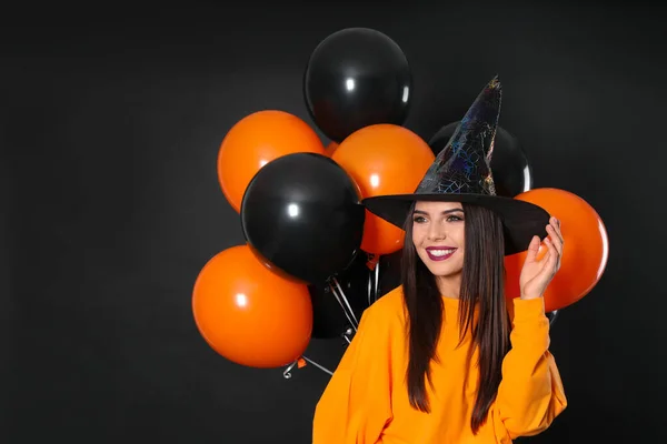 Mulher bonita vestindo traje de bruxa com balões para festa de Halloween no fundo preto — Fotografia de Stock