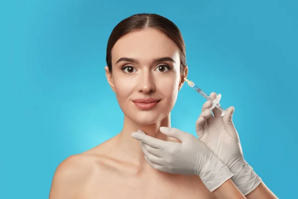 Krásná žena dostat injekci obličeje na světle modrém pozadí. Kosmetická chirurgie — Stock fotografie