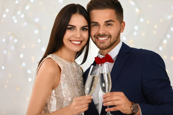 Schönes junges Paar mit Champagnergläsern gegen verschwommenes festliches Licht. Weihnachtsfeier — Stockfoto