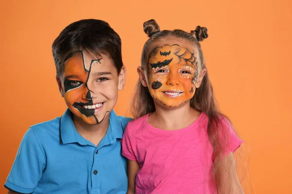 Lindos niños pequeños con pintura facial sobre fondo naranja — Foto de Stock