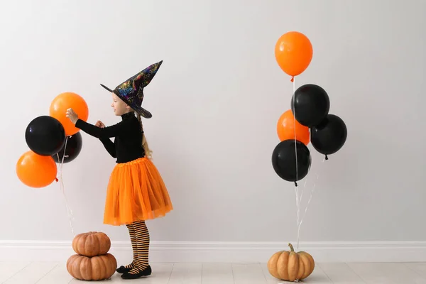 Roztomilá holčička s balónky a dýně na sobě halloweenský kostým v blízkosti světlé stěny — Stock fotografie