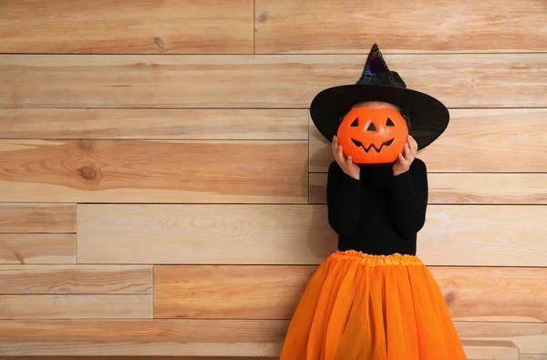 Jolie petite fille avec seau de bonbons à la citrouille portant un costume d'Halloween sur fond en bois. Espace pour le texte — Photo