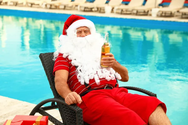 Tatil köyünde havuz kenarında bira şişesi olan otantik Noel Baba. — Stok fotoğraf
