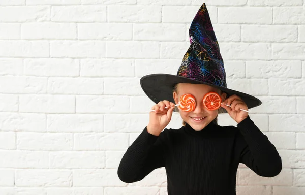 Roztomilá holčička s cukrovinkami v kostýmu Halloweena u zdi z bílých cihel. Mezera pro text — Stock fotografie