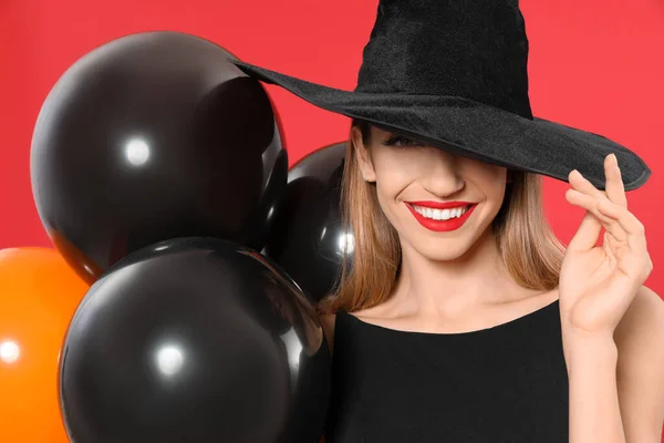 Schöne Frau trägt Hexenkostüm mit Luftballons für Halloween-Party auf rotem Hintergrund — Stockfoto