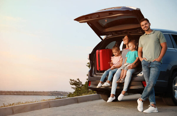 Счастливая молодая семья сидит в багажнике машины на берегу реки

