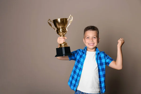 Happy boy met gouden winnende beker op beige achtergrond — Stockfoto