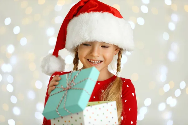 Criança feliz em chapéu de Papai Noel com caixa de presente contra luzes festivas borradas. Celebração de Natal — Fotografia de Stock