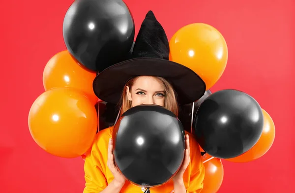 Hermosa mujer con traje de bruja con globos para la fiesta de Halloween sobre fondo rojo —  Fotos de Stock