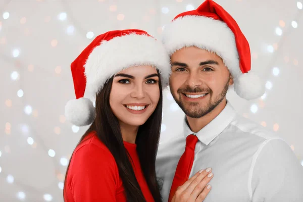 산타 모자를 쓴 사랑 스런 젊은 커플 이 화려 한 축제의 불빛을 막고 있습니다. 크리스마스 축하 — 스톡 사진