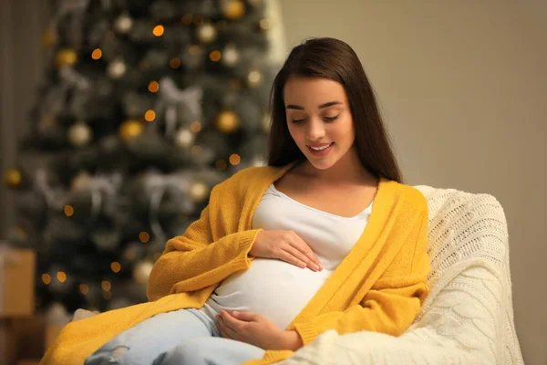 Mulher grávida feliz em poltrona no quarto decorado para o Natal. Bebê esperado — Fotografia de Stock