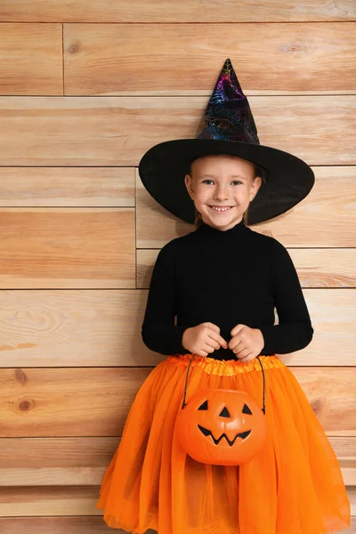 Carino bambina con zucca secchio di caramelle indossando costume di Halloween su sfondo di legno — Foto Stock