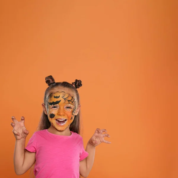 Linda niña con pintura facial sobre fondo naranja. Espacio para texto — Foto de Stock