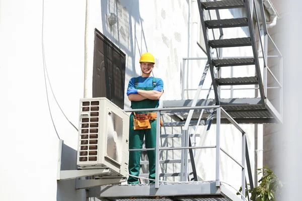 Joven técnico masculino cerca de aire acondicionado moderno al aire libre — Foto de Stock