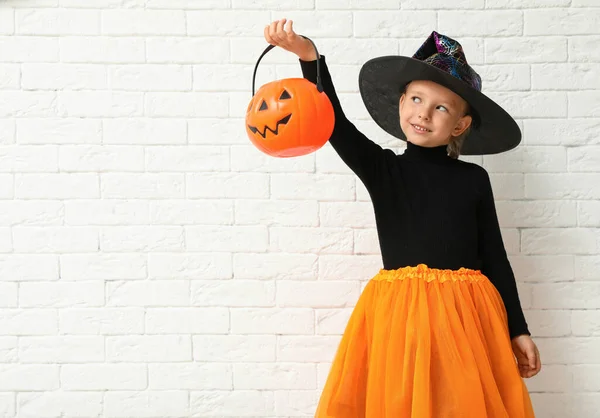 Cute little girl z dyni Candy Bucket noszenie kostium Halloween w pobliżu białej cegły ściany. Miejsce na tekst — Zdjęcie stockowe