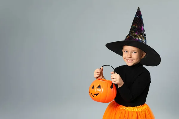 Cute little girl z dyni Candy wiadro sobie kostium Halloween na szarym tle, miejsce na tekst — Zdjęcie stockowe