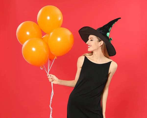 Gyönyörű nő visel boszorkány jelmez léggömbökkel Halloween party piros háttér — Stock Fotó