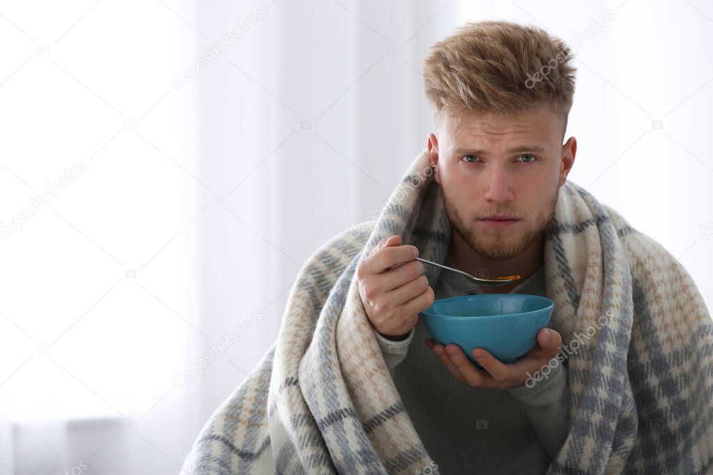 Sick young man eating soup to cure flu at home. Space for text