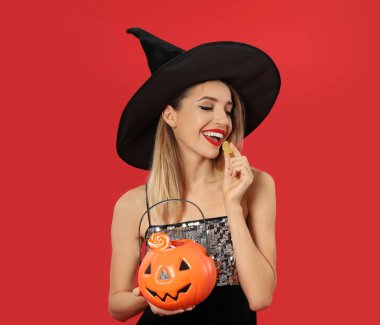 Kırmızı arka planda Jack O 'Lantern şeker kabı olan cadı kostümü giyen güzel bir kadın. Mesaj için yer var. Cadılar Bayramı partisi