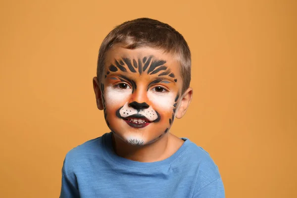 Lindo niño con pintura facial sobre fondo naranja — Foto de Stock