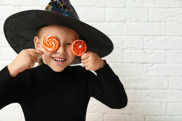 Petite fille mignonne avec des bonbons portant un costume d'Halloween près du mur de briques blanches. Espace pour le texte — Photo