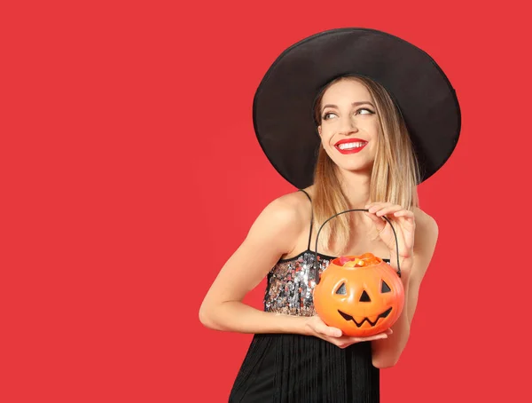 Hermosa mujer con traje de bruja con Jack O 'Lantern contenedor de caramelos sobre fondo rojo, espacio para el texto. Fiesta de Halloween —  Fotos de Stock
